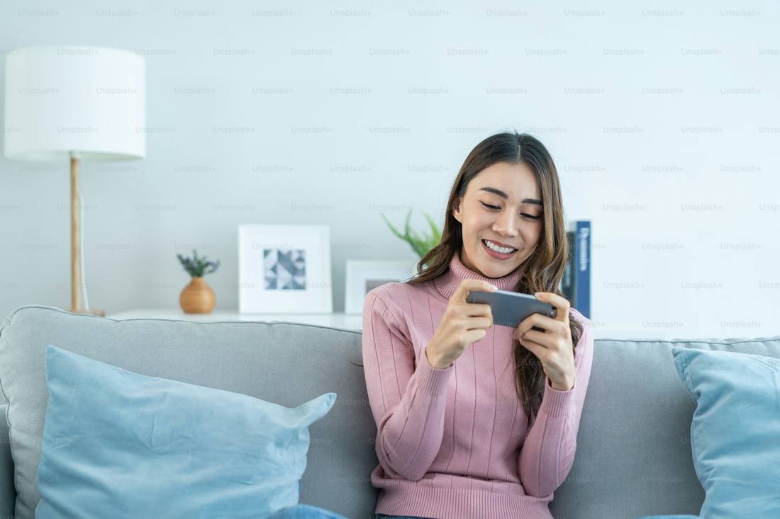 Pengguna menikmati permainan dari smartphone di sofa